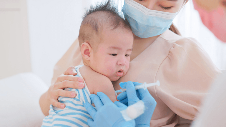 Healthcare worker administers a routine vaccine to an infant while a caregiver holds the child.