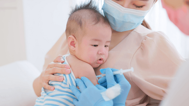 Healthcare worker administers a routine vaccine to an infant while a caregiver holds the child.