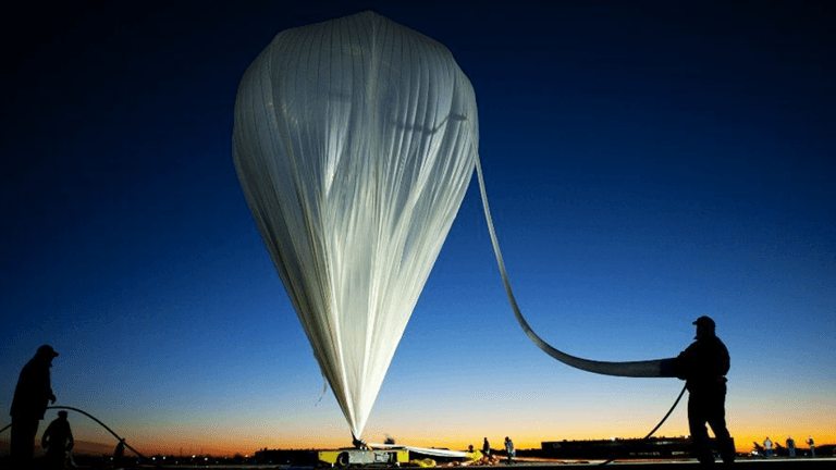 A large white weather balloon is being prepared against a vibrant sunset sky.