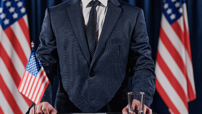 A man in a suit stands at a podium with American flags behind him