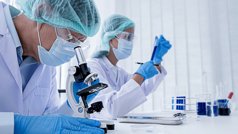 Scientists in lab coats using a microscope and pipette in a laboratory setting