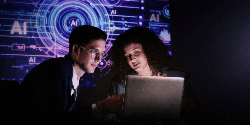 AI Investment Remains a Driving Force for Global Markets as Earnings Season Begins Two professionals collaborate on a laptop with AI graphics displayed on digital screens in the background.