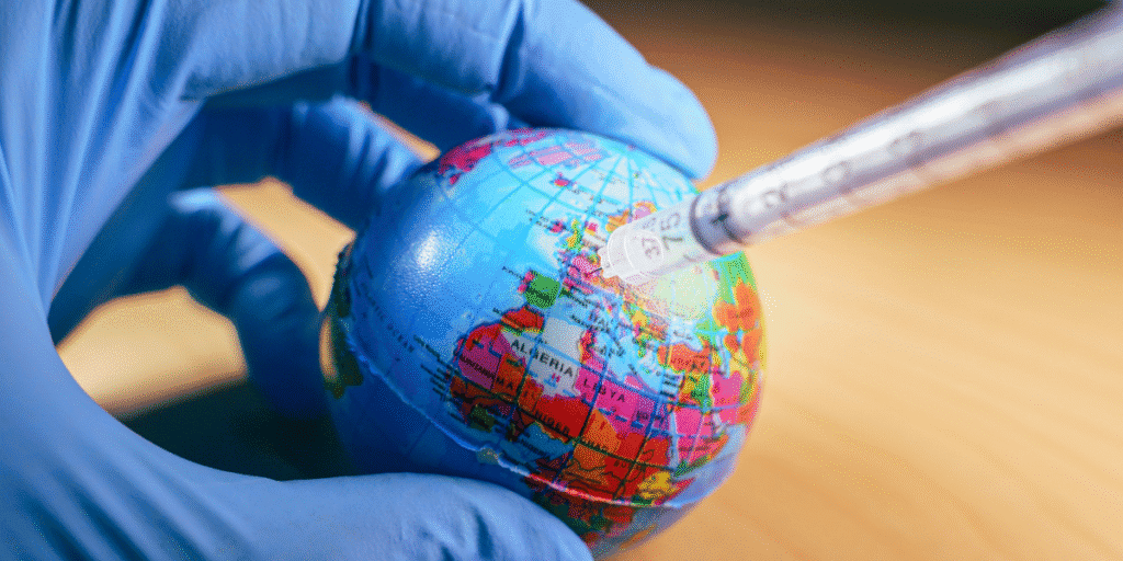 Gloved hand holding a globe while a syringe points toward it, symbolizing global vaccination.